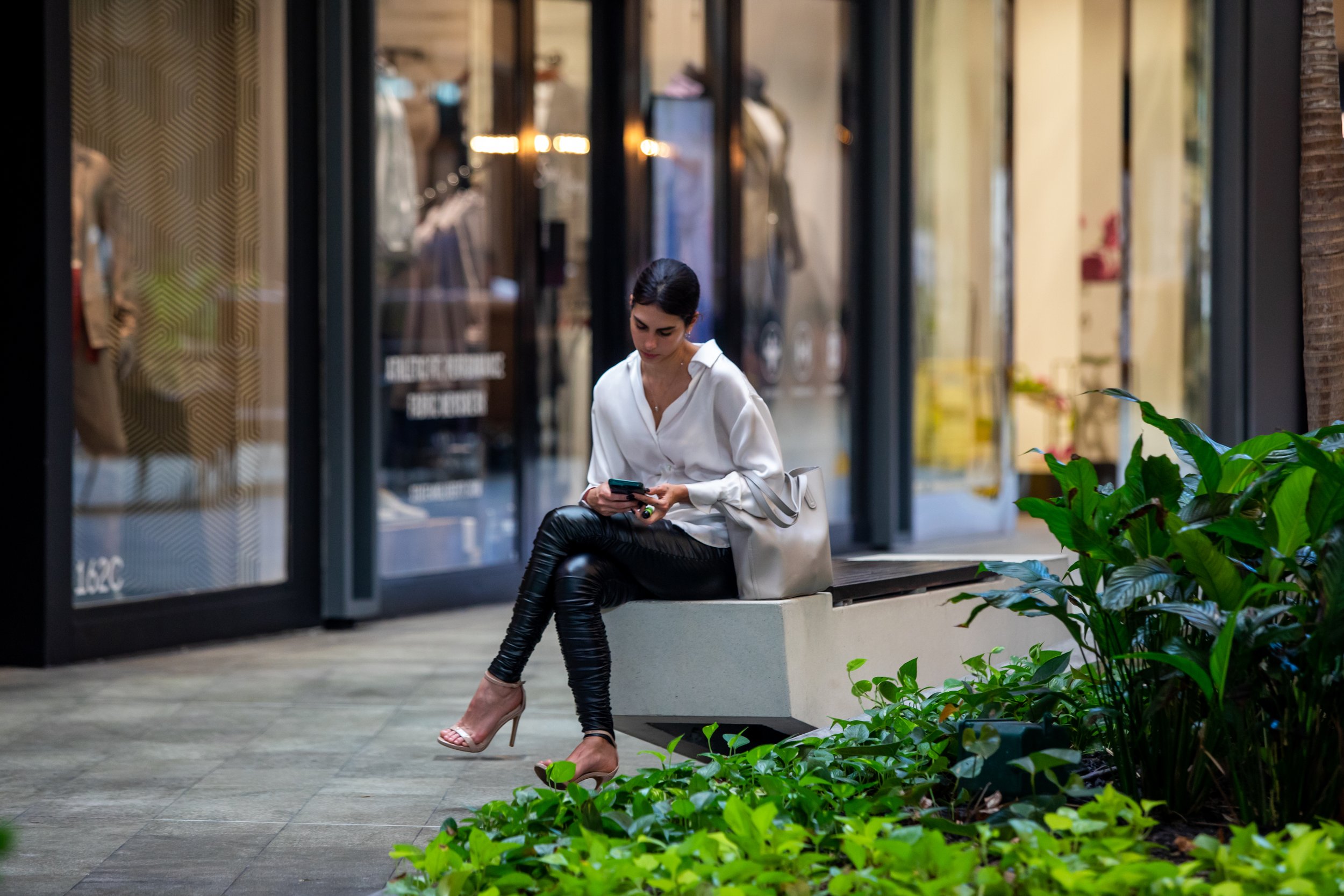 Woman looking at phone in a mall with high-end dresses in the background